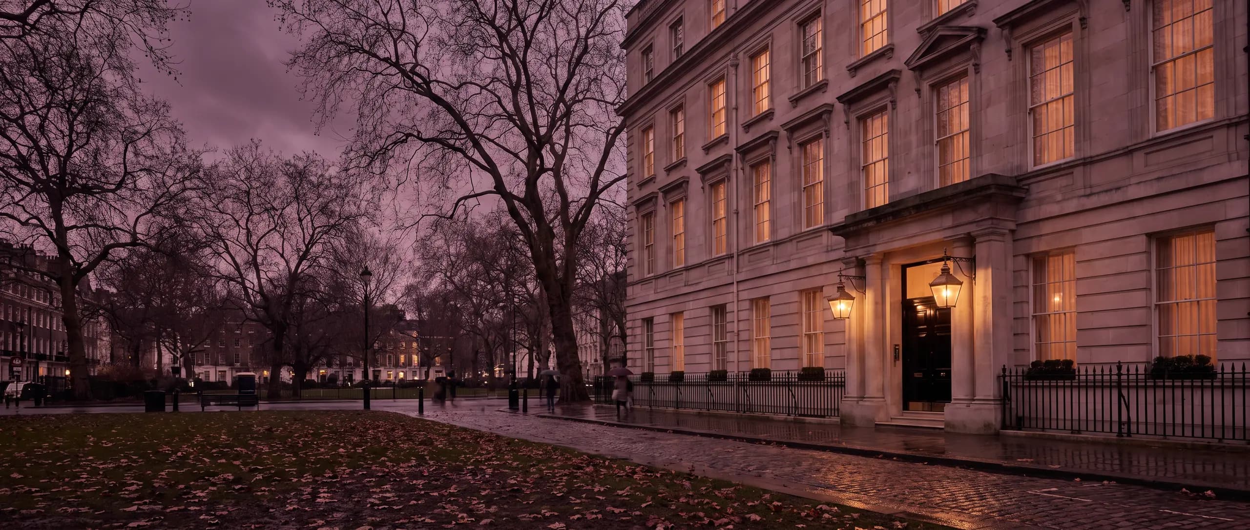 The Portland-stone front of Lavenhall at dusk, its sash windows lit across a wet Mayfair garden square